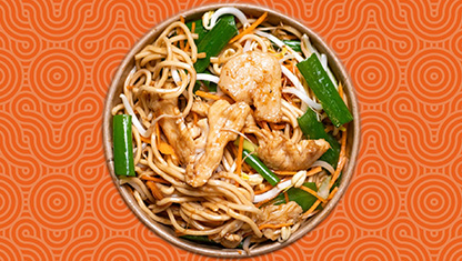 En tallrik med nudlar och kyckling med grönsaker. Bakgrunden är orange.