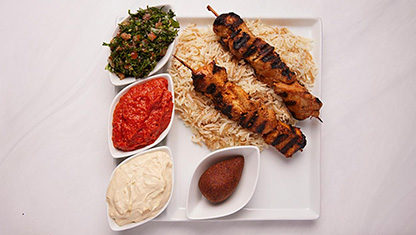 Fyra stycken mezas, två grillspett och ris serverat på en tallrik. 