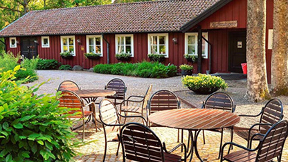 Utanför Kaffestugan i Apladalen med utemöbler och den röda stugan i bakgrunden.